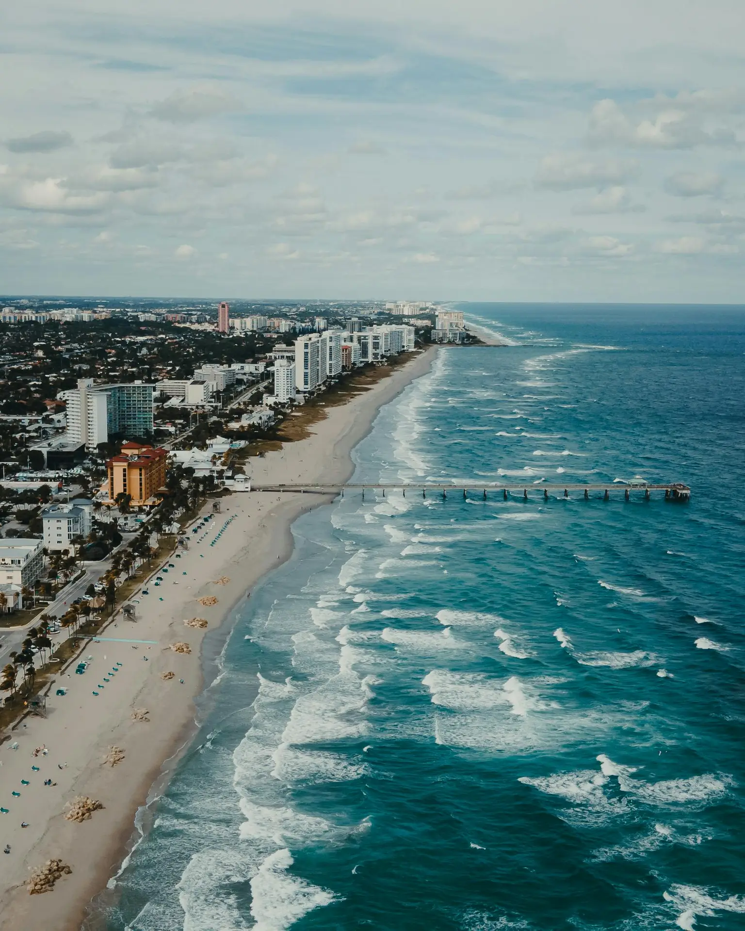 A stunning aerial view of a beachfront cityscape with a long pier and turquoise waves.